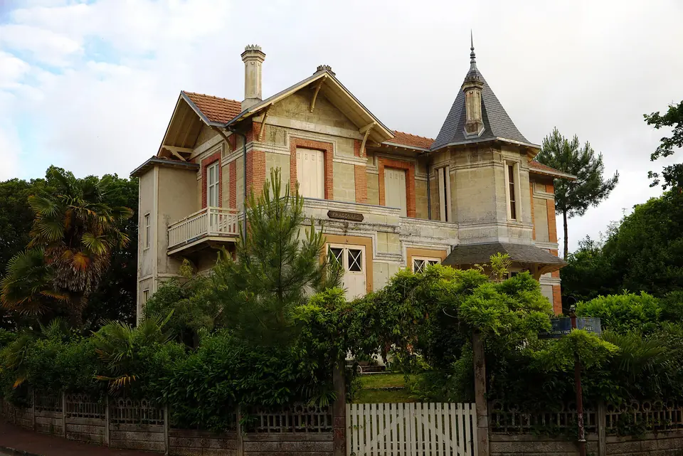 Villa Fragonard à Arcachon, maison de villégiature à tourelle, balcons en bois et toits pentus, entourée d'arbres et de végétation.
